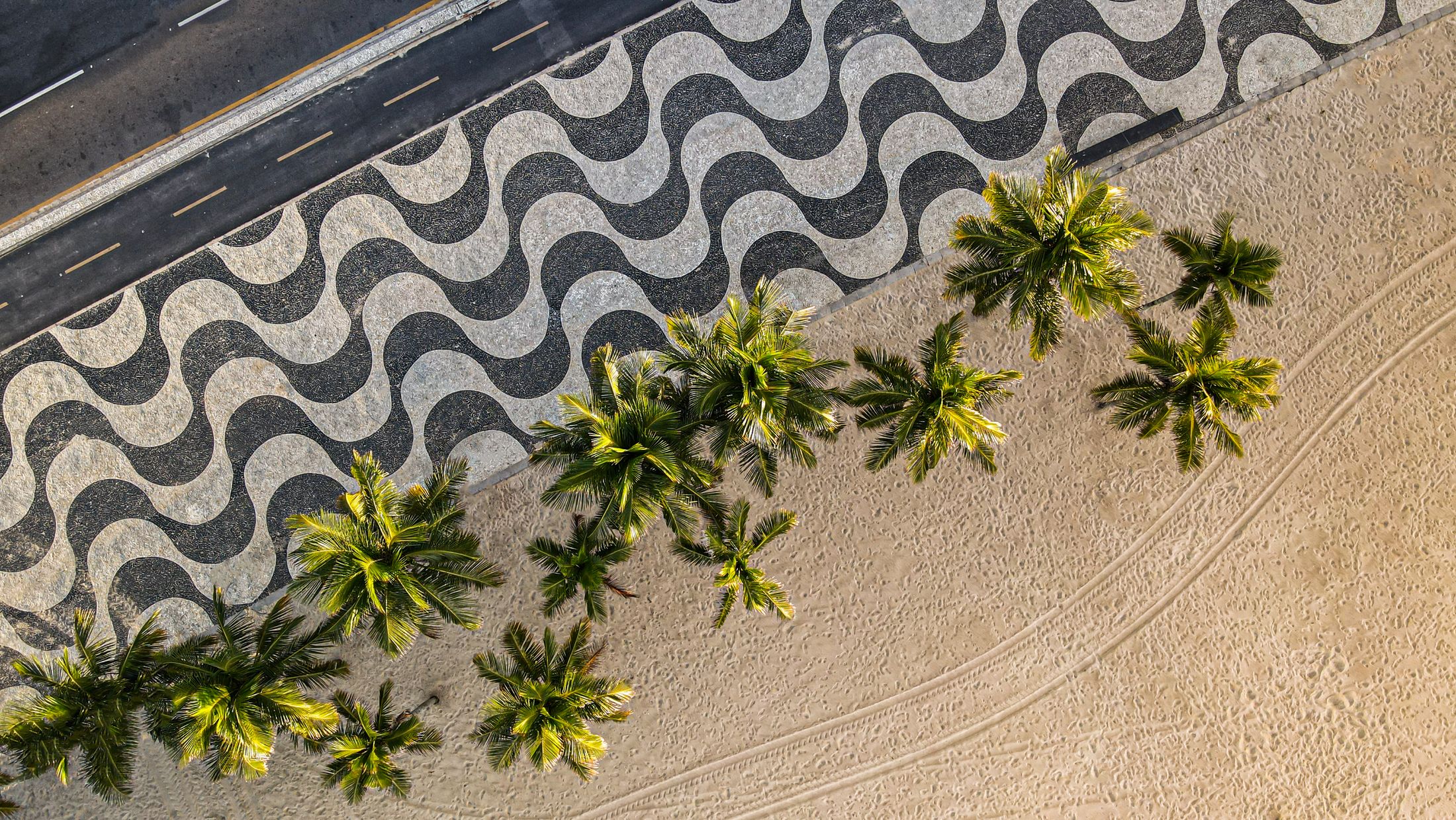 Calçadão de Copacabana visto de cima, com o desenho de ondas em pedra preta e branca e coqueiros